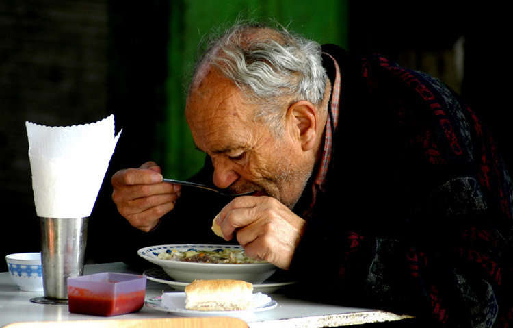 Comer. Hombre tomando su comida. Barrio Patronato, Santiago, Chile.